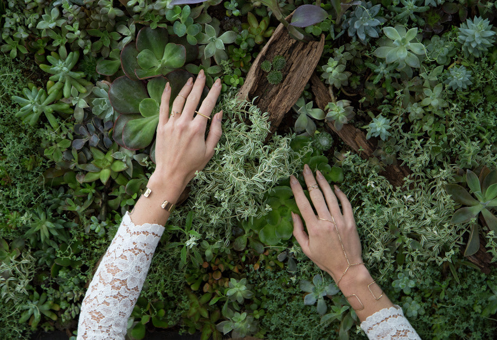 model with arms on greenery wall wearing Alexis Russell jewelry