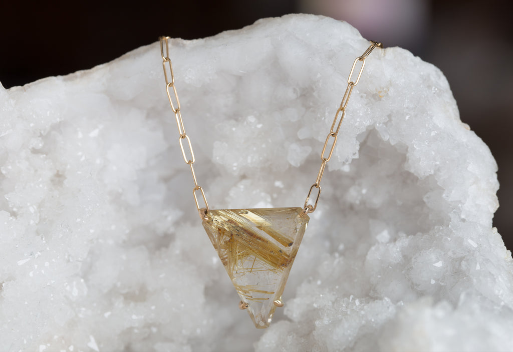 yellow gold rutilated quartz pendant necklace draped over white druzy crystal