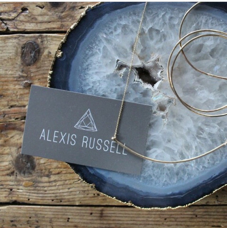 Gold Necklace and black Alexis Russell business card laying on blue slice agate