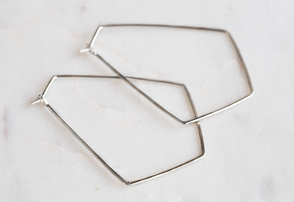 White Gold Hexagon Hoop Earrings on white marble tile