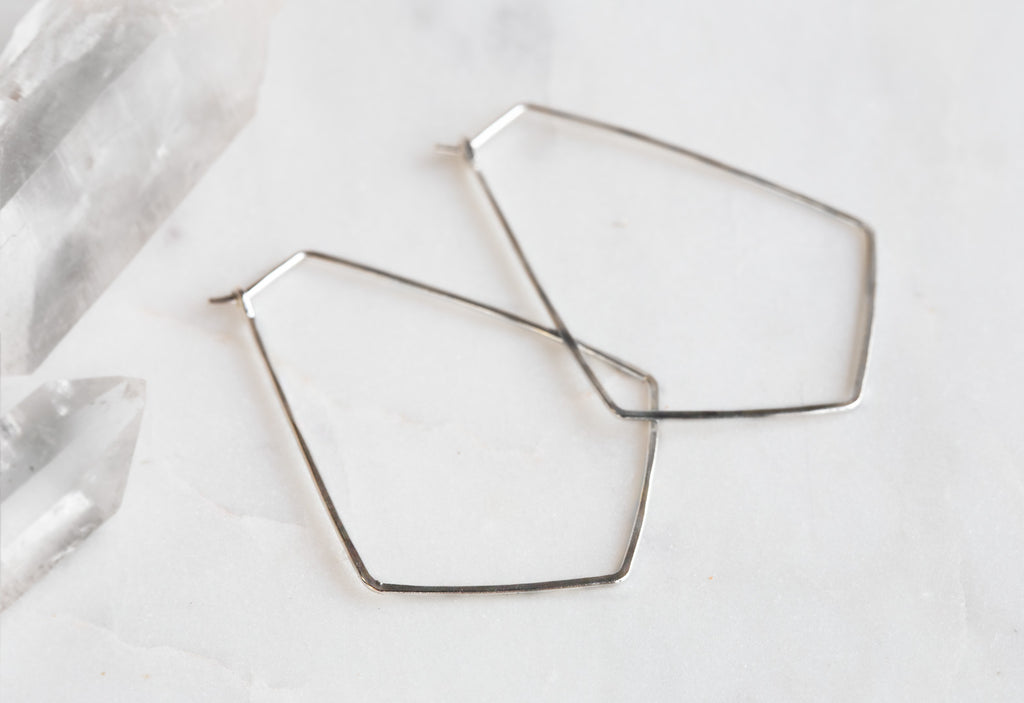 White Gold Hexagon Hoop Earrings on white marble tile