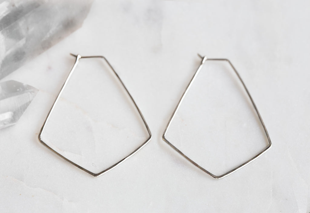 White Gold Hexagon Hoop Earrings on white marble tile