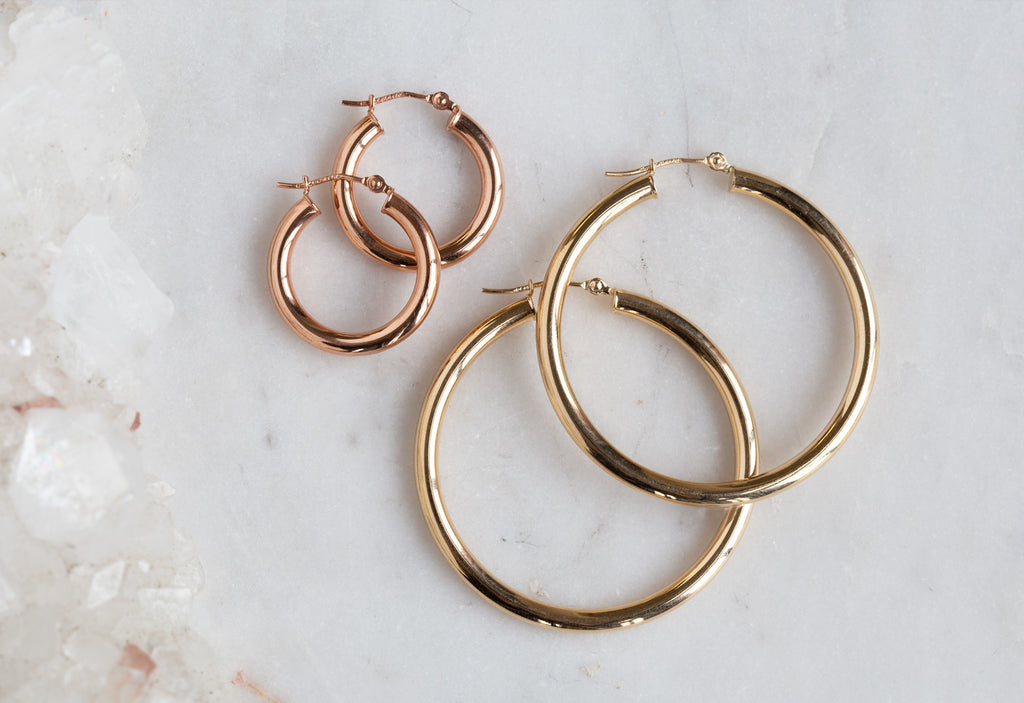 small rose gold hoop earrings and large yellow gold hoop earrings on white marble tile