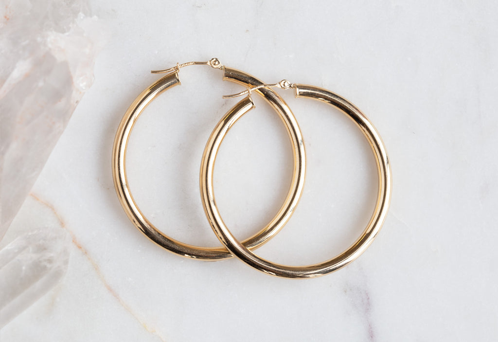 Large Yellow Gold Hoop earrings on white marble tile