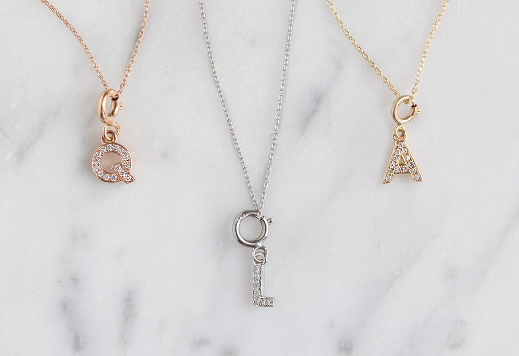 "Q" "L" and "A" pavé diamond charm necklaces on marble