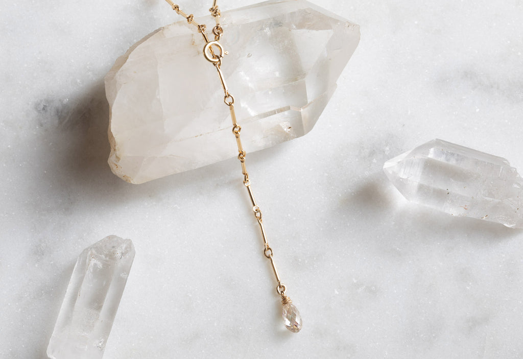yellow gold champagne diamond lariat necklace laying on white crystal