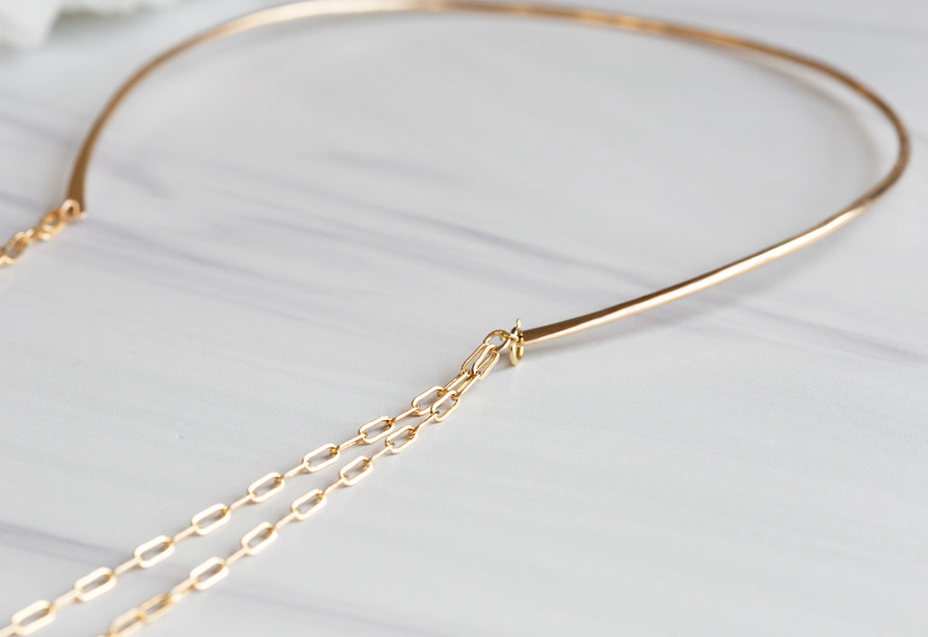 Close Up of Yellow Gold Chained Open Cuff Necklace on White Marble Tile