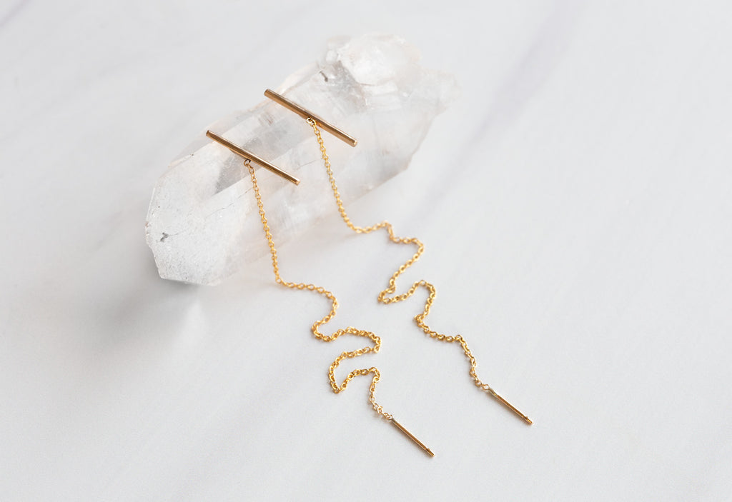 Linea Thread Earrings laying on hexagonal white crystal