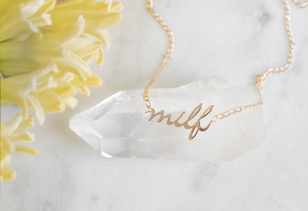 'Milf' Necklace laying on white hexagonal crystal with yellow flowers off to the side