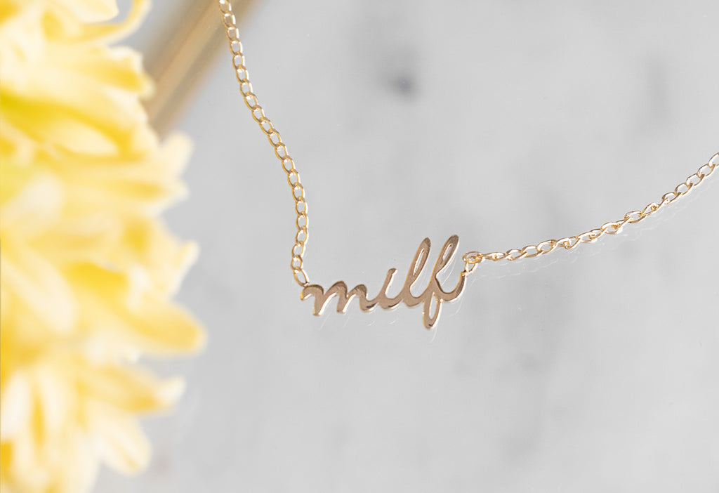 yellow gold 'Milf' necklace on glass box with yellow flower next to it